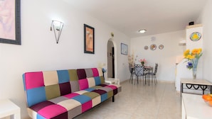 A living room with a colorful sofa, a dining table with chairs, and a vase with flowers. - 1 Bed Hotel Apt. in Costa Adeje, Few minutes walk to Beach, Shops & Restaurants (Costa Adeje)
