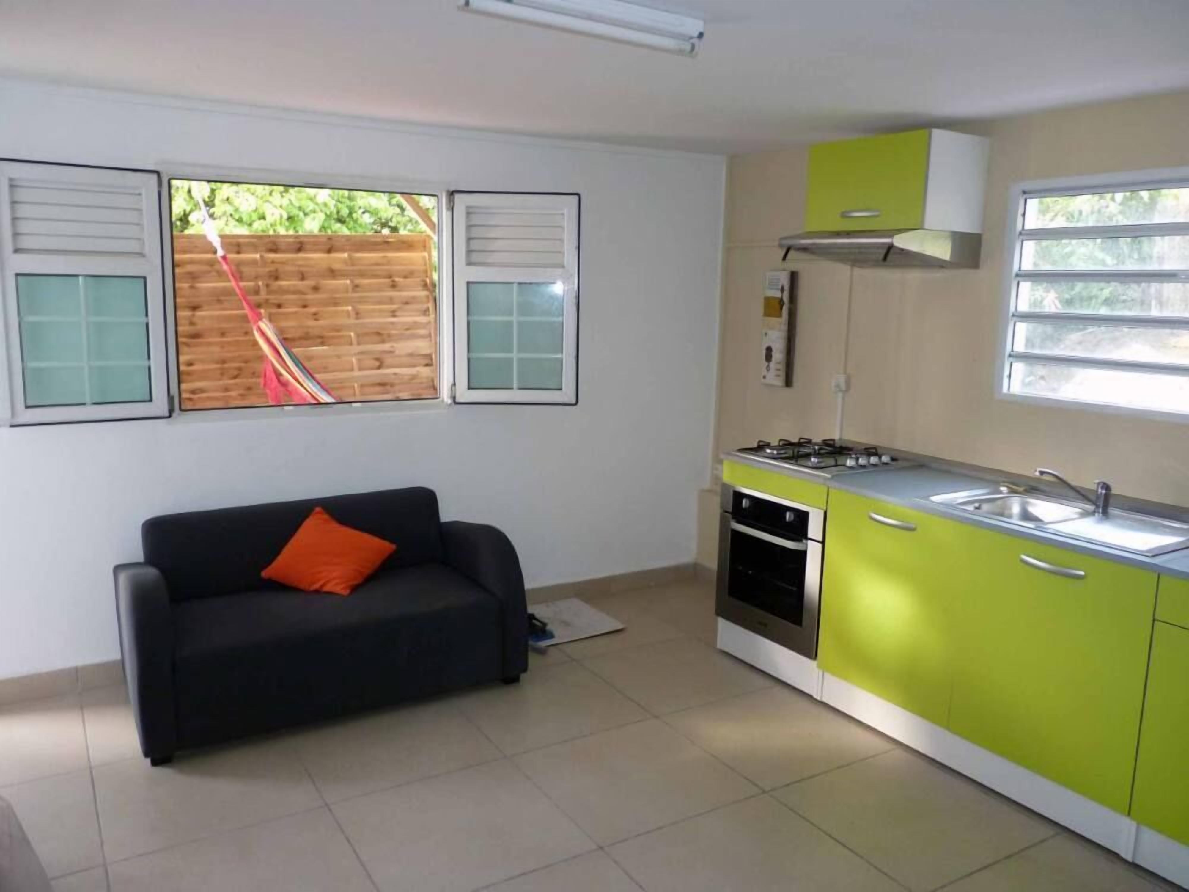 Une cuisine compacte équipée d’une cuisinière à gaz, d’un four et d’un évier, située à côté d’un canapé noir agrémenté d’un coussin orange.