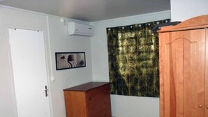 Ein Zimmer mit einer weißen Tür, einem Holzschrank, einer Wand-Klimaanlage und einem gemusterten Vorhang.