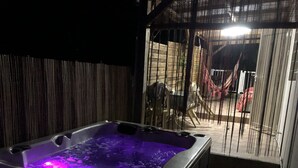 Ein Whirlpool mit violetter Beleuchtung, umgeben von einem Bambuszaun und einer Hängematte.