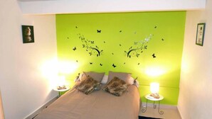 Ein kleiner, heller Raum mit einem Bett, zwei Nachttischen und einer grünen Wand mit Schmetterlingsmotiven.