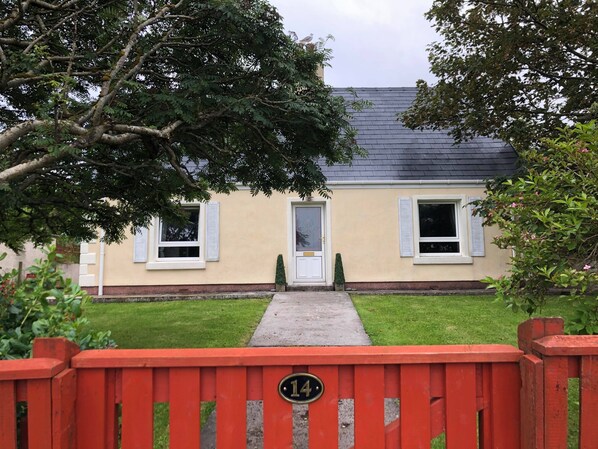 A house with a number 14 sign on a red gate, a front door, and two windows with shutters.