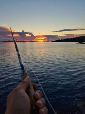 A fishing rod held over calm water during sunset.