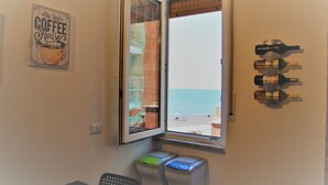 A room with a window overlooking the sea, a coffee-themed wall art, and a wall-mounted wine bottle rack.