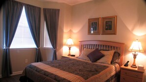 Un lit bien fait, recouvert d’une couvre-lit à motifs, deux lampes de chevet, une table de chevet avec une télécommande, et deux tableaux encadrés accrochés au mur.