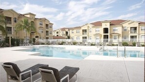 Un espace piscine avec des chaises longues et un bâtiment doté de nombreux balcons.