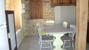 Un comedor con pared de piedra, vigas de madera en el techo y una mesa blanca con cuatro sillas.