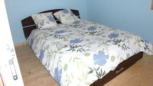 Una cama individual con una colcha estampada floral en una habitación con paredes azul claro y suelo de madera.