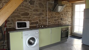 Una cocina con pared de piedra, lavadora, microondas y fregadero.