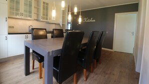A modern kitchen with a dining table and chairs, wooden cabinets, and pendant lights.