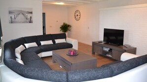 A modern living room with a sectional sofa, a coffee table, a flat-screen TV, and a clock on the wall.