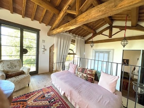 Un dormitorio acogedor con techo de madera, cama con ropa de cama estampada, una silla y una alfombra colorida.