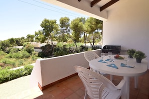 A balcony with a table set for two, a grill, and a view of trees and buildings.
