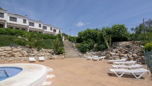 A pool area with lounge chairs, a stone wall, and a staircase leading to a building.