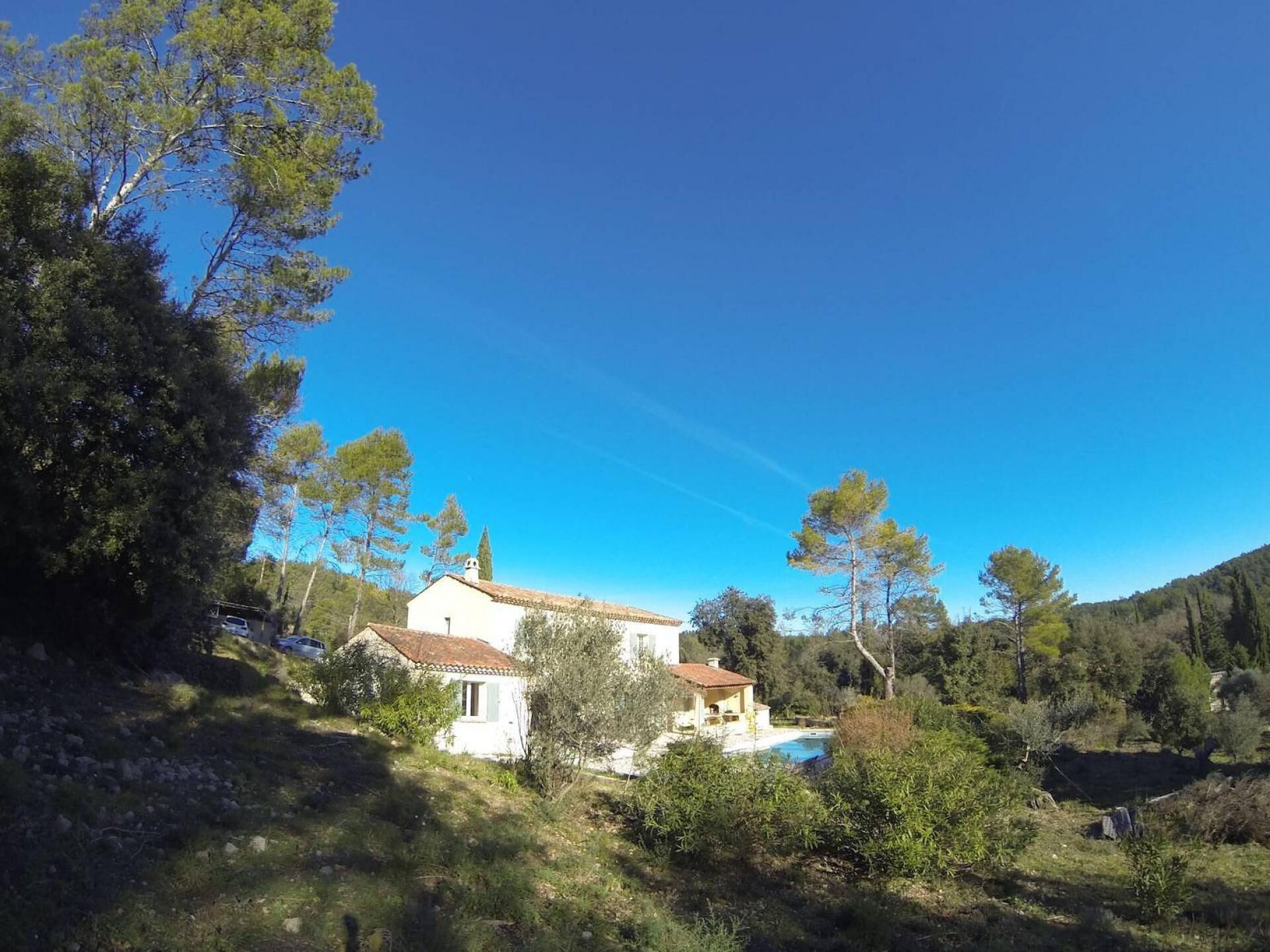 A white villa with a tiled roof, surrounded by trees and a clear blue sky.