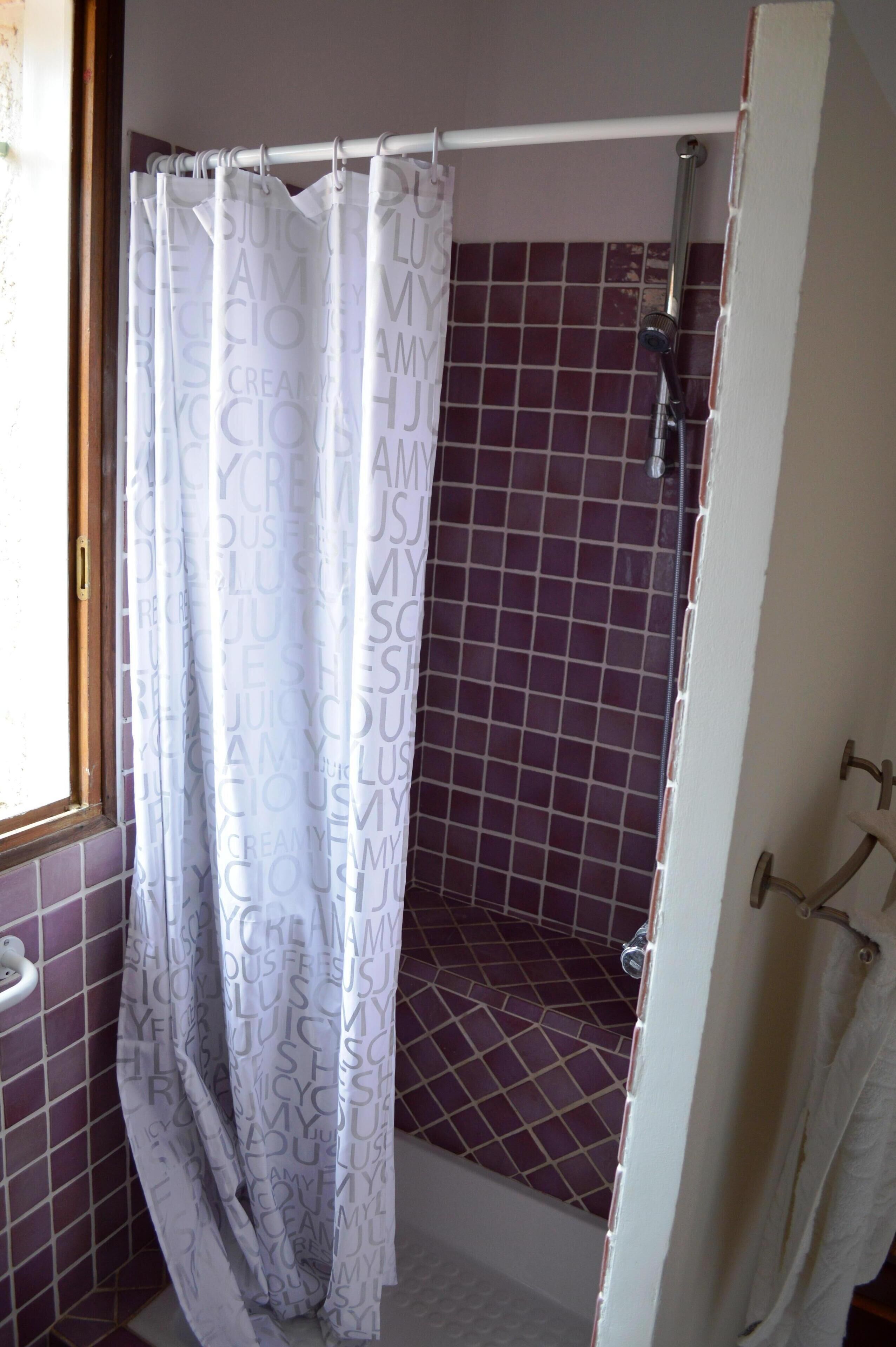 A bathroom with purple-tiled walls, a shower with a white curtain, and a visible towel rack.