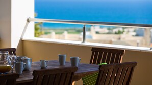 A table with a view of the ocean, a glass pitcher, and several cups.