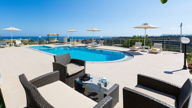 A poolside area with lounge chairs and umbrellas, overlooking a clear blue sky and a distant view.