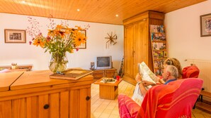 Una sala de estar acogedora con muebles de madera, un televisor, una estantería y un florero con flores.