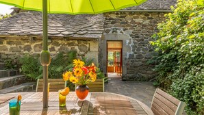 Un patio con una mesa, sillas, un paraguas verde y un edificio de piedra al fondo.