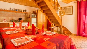 Un comedor con una larga mesa dispuesta para una comida, una cocina al fondo y una escalera de madera.