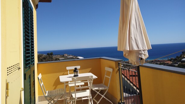 Een balkon met een tafel, stoelen, een parasol en uitzicht op zee.