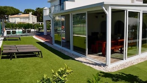 Une maison moderne dotée d’un patio entièrement vitré, d’un espace salon extérieur et d’une pelouse bien entretenue.