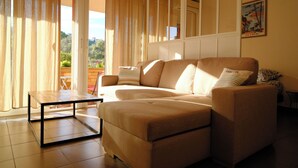A living room with a sofa, a coffee table, and a view through large windows. - Studio - Porto Vecchio (Porto-Vecchio)