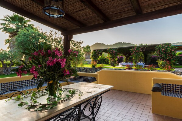 An outdoor patio with a table and chairs, surrounded by lush greenery and a view of a landscaped garden. - Chateaux Lemon, lush garden, charming pool in the lemongrove, dreamy countryside (trappitello)