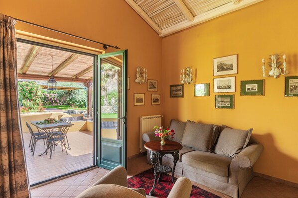 A cozy living room with a sofa, a small table with a vase of flowers, and a dining area with chairs and a table.
