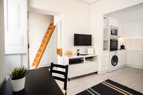 Une cuisine moderne avec des meubles blancs, un lave-linge encastré et un téléviseur à écran plat.