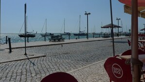 Eine Kopfsteinpflaster-Uferpromenade mit angestaubten Booten, Laternen und Sitzgelegenheiten im Freien.