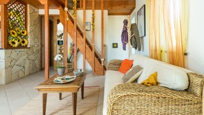 Una sala de estar acogedora con una escalera de madera, un sofá con cojines, una mesa de centro y un perchero en la pared.