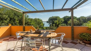 Un patio al aire libre con una mesa y sillas de madera, rodeado de paredes anaranjadas y vistas a árboles y agua.