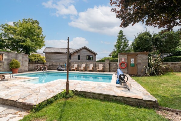 A backyard with a swimming pool, stone patio, and a small wooden shed.