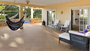 Eine überdachte Terrasse mit einer Hängematte, zwei Liegestühlen und einem Korbsessel-Sofa.