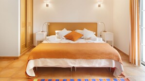 Ein ordentlich bezogenes Bett mit weiß-orangefarbener Tagesdecke, zwei Nachttischlampen und einem hölzernen Kopfteil.