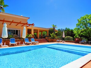 A clear blue pool with lounge chairs and umbrellas, surrounded by a stone wall and a building with a tiled roof. - PEACEFUL COZY COMFORTABLE SUNNY VILLA (PRAIA DO CARVOEIRO, LAGOA)