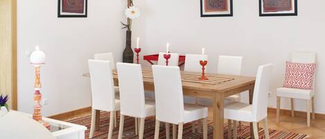 A dining room with a wooden table, white chairs, and a patterned rug.