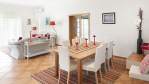 Ein Essbereich mit einem Holztisch und weißen Stühlen, einem gemusterten Teppich und einem weißen Sofa im Hintergrund.