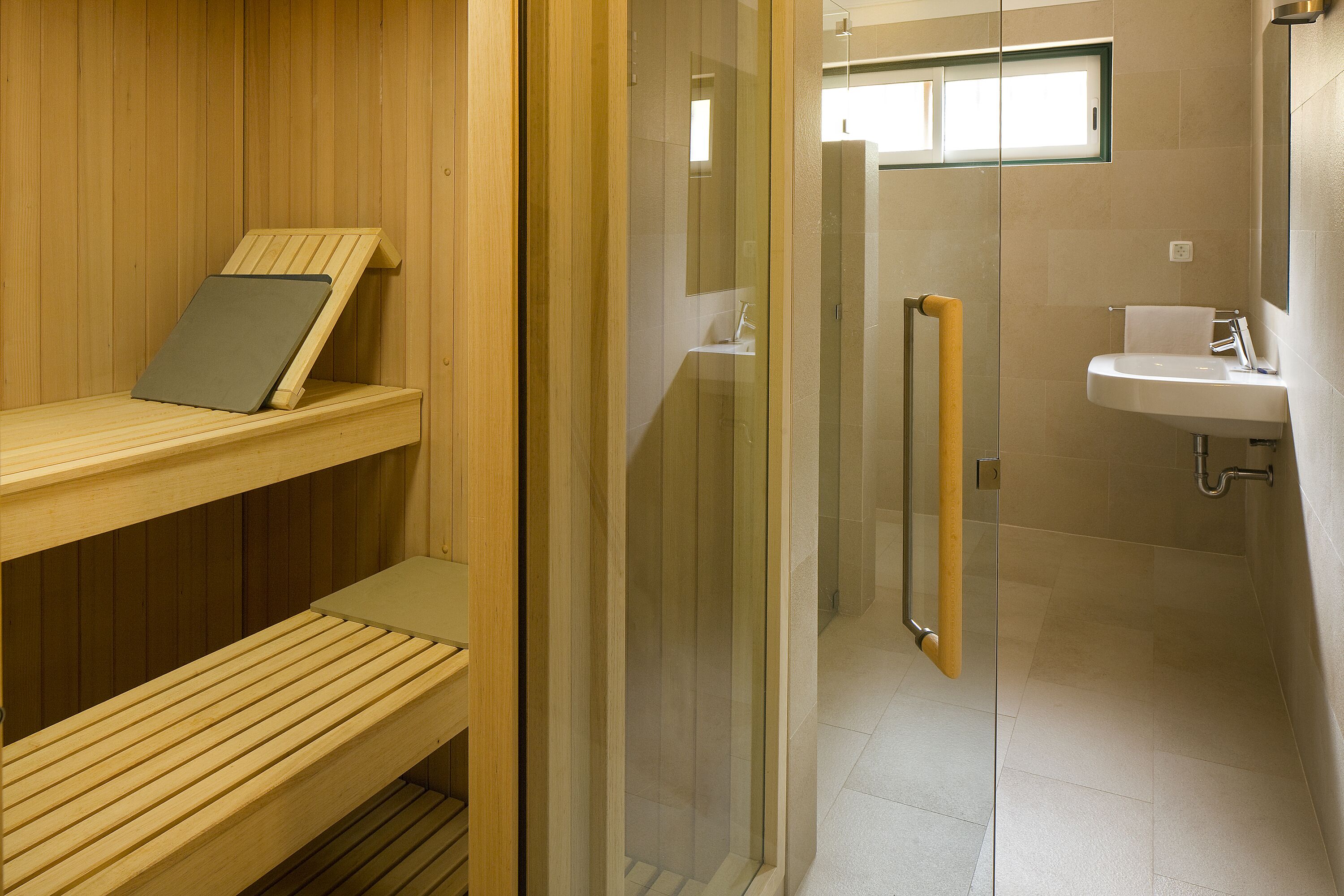 A sauna with wooden benches and a glass door leading to a shower area with a sink and mirror.
