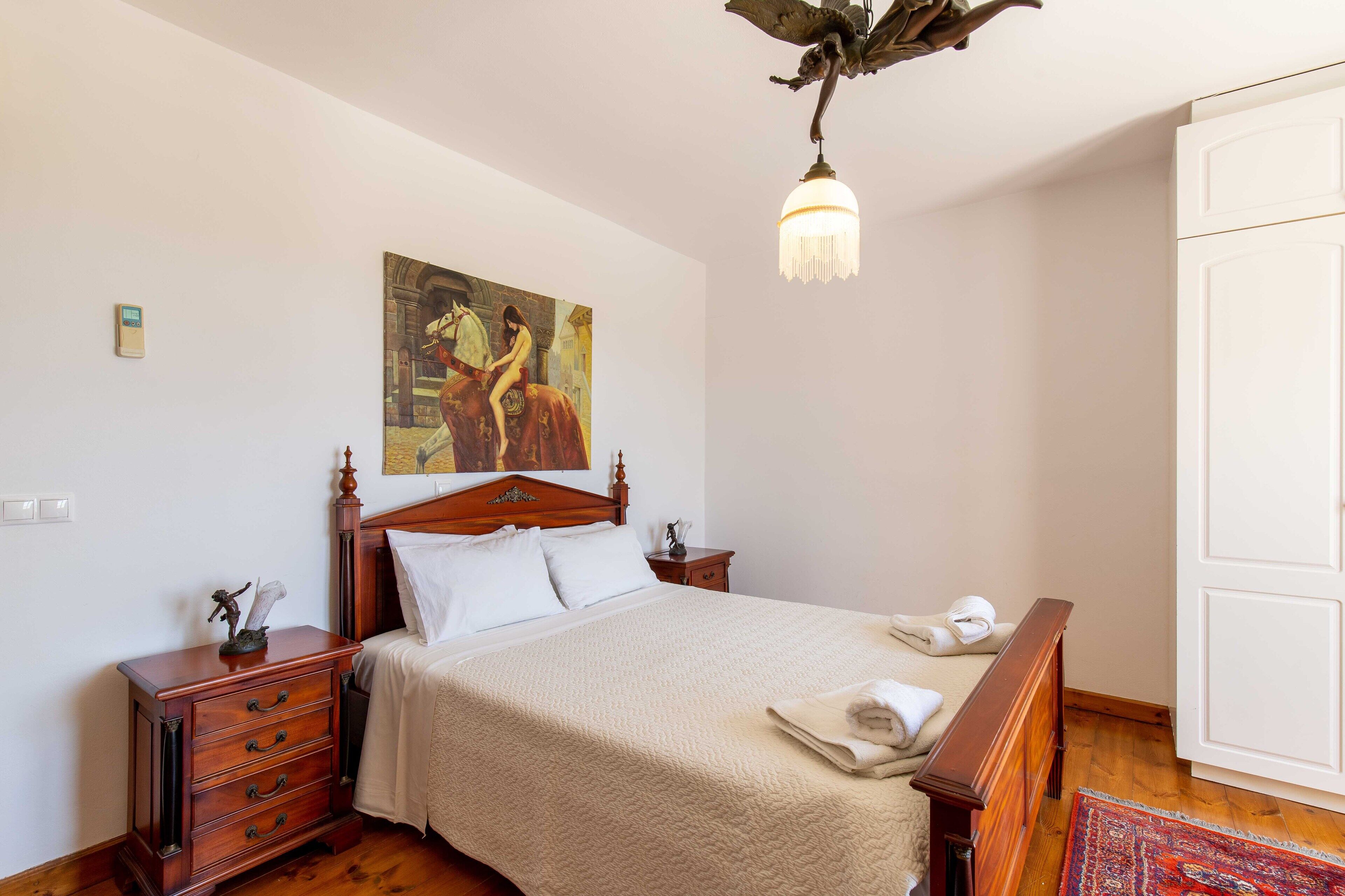 A neatly made bed with a wooden headboard, a bedside table with a lamp, and a painting on the wall.