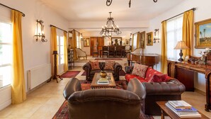Een ruime woonkamer met een open haard, leren banken, een salontafel en een kroonluchter.