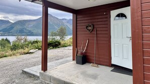 Un edificio de madera con puerta blanca, un porche y vistas a montañas y un lago.
