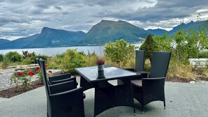 Mesa y sillas al aire libre con vista a montañas y un lago.
