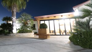 A modern building with a large glass entrance, surrounded by palm trees and a stone wall. - B&B room with swimming pool (Gasponi)