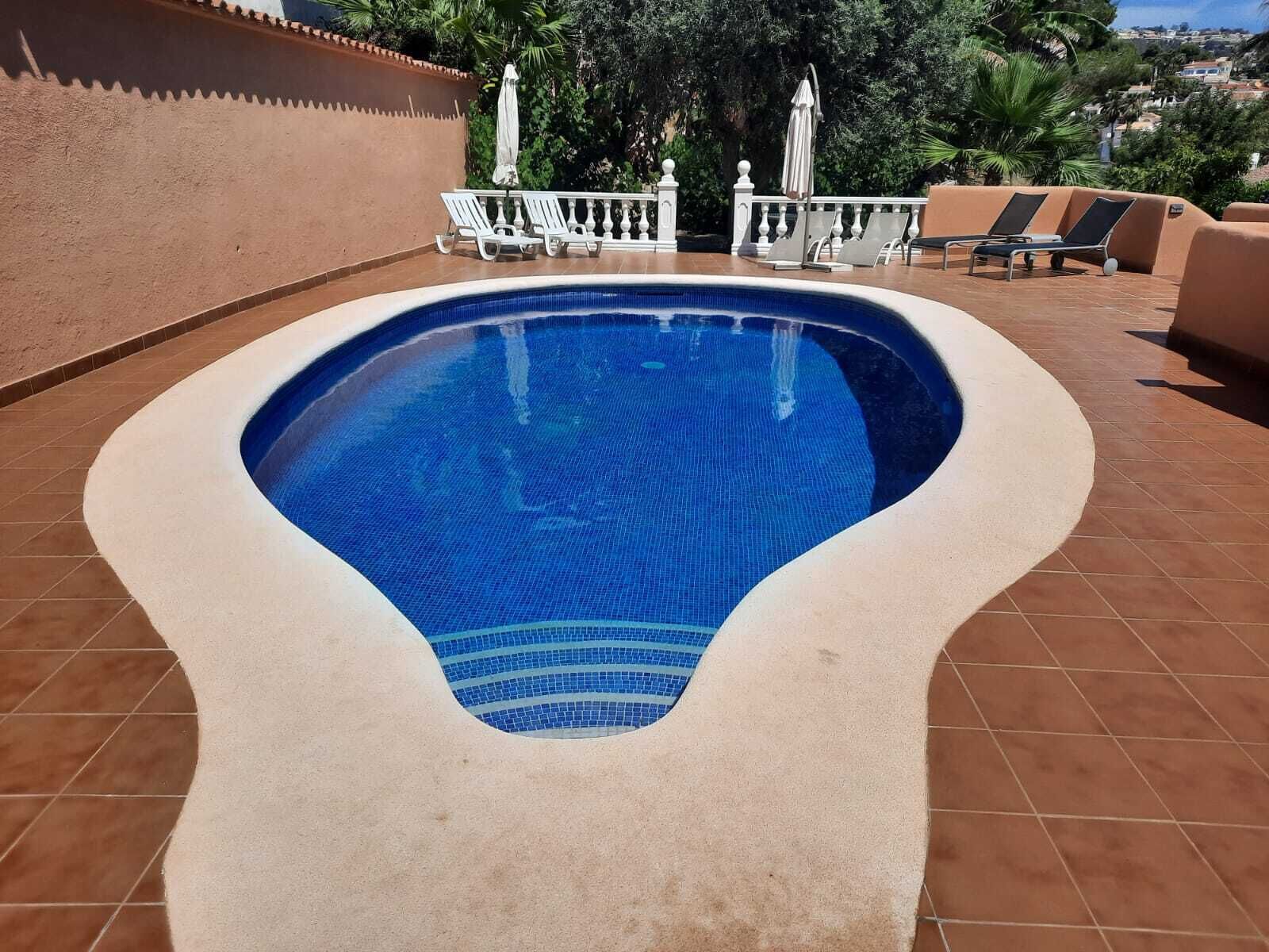 Una piscina de forma singular, rodeada por una solana con baldosas y barandillas blancas.