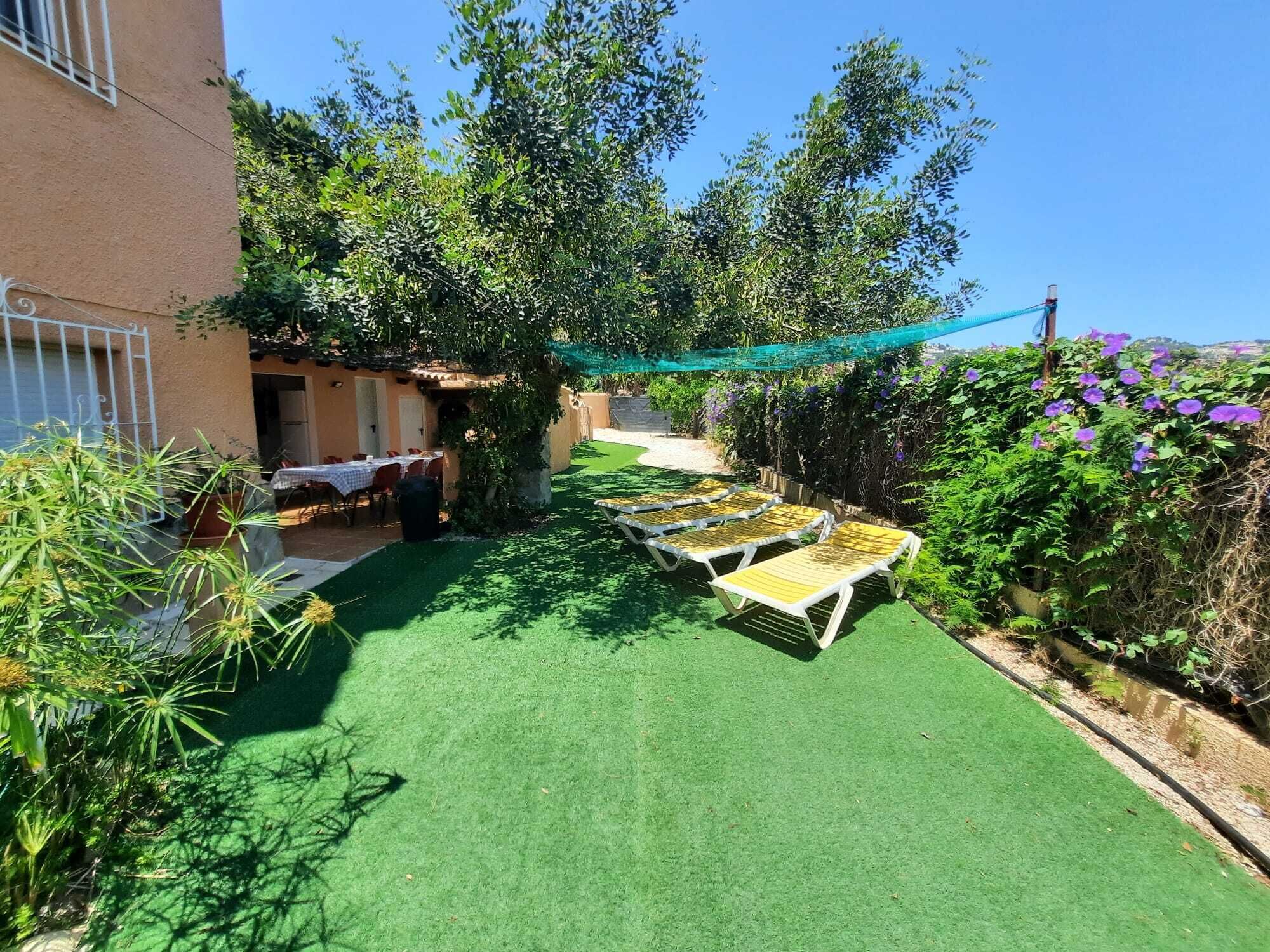 Un patio con mobiliario exterior, césped verde y vegetación circundante.