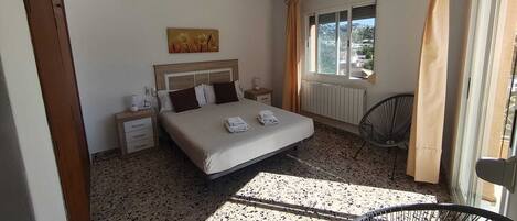 A bedroom with a bed, bedside tables, a ceiling fan, a window with curtains, and a radiator.