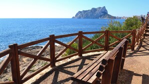 A wooden bench and railing overlooking a coastal area with a rocky shoreline and a mountain in the distance.